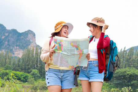 Portrait of two Asian female travelers carrying backpacks Standing looking at map to travel nature. Cheerful smile. Happy. Travel concept. Tourists hiking, camping.の写真素材