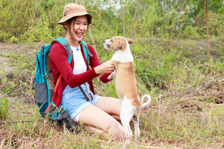 Beautiful Asian female traveler in hat sitting on floor playing with dog. She smiles cheerfully, happy. Travel concept. hikers, petsの写真素材
