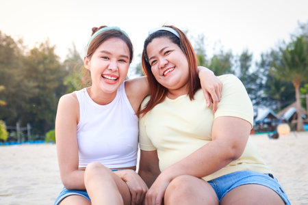 Two fat and skinny asian girls having fun enjoying sea tourism Sitting on the beach, hugging his neck, smiling happily. Travel woman. Travel and lifestyle conceptの写真素材