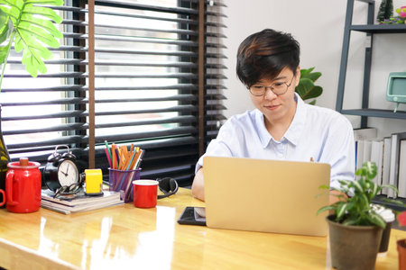 Asian woman with short hair wearing eyeglasses sites working with laptop computer in home office. personal business. freelance.の写真素材