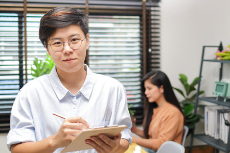 Asian woman with short hair wearing eyeglasses holding a work notebook. personal business. Freelance, entrepreneur conceptの写真素材
