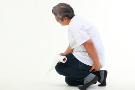 Asian fat man sitting on white floor holding toilet paper He used his other hand to hold his buttocks. The concept of health care for obese people. hemorrhoidsの写真素材