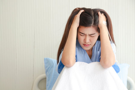 Stressed Asian female patient holding her head in a hospital bed. Taking out health insurance. women's health problemsの写真素材