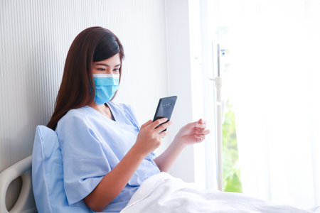 Asian female patient using smartphone during hospital treatment. Taking out health insurance. women's health problemsの写真素材