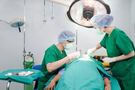 An Asian medical team performs facial surgery on a female patient lying on an operating room bed. Beauty concept. Medical services in hospitals. Surgeon. Emergency accident.の写真素材