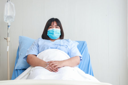 Portrait of an obese female patient in a mask lying on a hospital bed. The concept of health insurance. disease of the obeseの写真素材