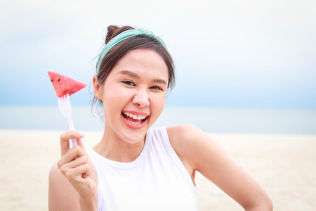 Young beautiful Asian smiling happy woman travels to the sea on vacation. holding a fresh red watermelon The taste is sweet, juicy, cool down, feel refreshed. travel conceptの写真素材