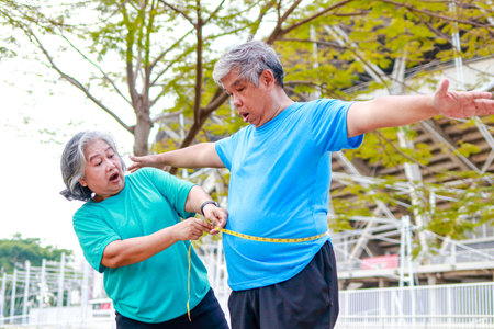 An elderly Asian woman measures the waist circumference of an elderly man with a tape measure. She was shocked by the size of her waist. Sports concept. Health care in retirement. obesity weight lossの写真素材