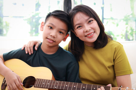 Portrait of Asian mother and son playing music together sitting on sofa in house. Music concept. Modern family activity.の写真素材