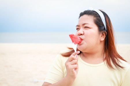 Asian fat woman happy Eat watermelon on the sea beach. Summer travel concept. copy spaceの写真素材