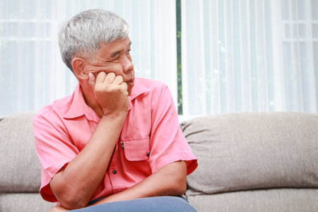 Asian elderly man having toothache sitting at the sofa in the house. An elderly man is stressed with life problems in retirement. copy spaceの写真素材