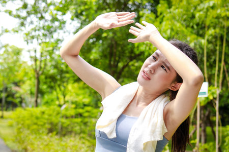 Asian woman exercising outdoors on a hot sunny day, body temperature above 40 degrees Celsius, using her hands to cover the sun. heat strokeの写真素材