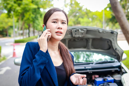 Beautiful Asian woman, broken car on the road Hold a smartphone to inform the insurance company to call for emergency assistance. Concept of car insurance. car service. transportationの写真素材