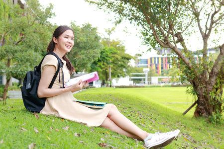 Asian female student sitting on the grass reading a book on the university campus. Education concept. copy spaceの写真素材