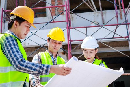 Architects, engineers and contractors holding construction drawings outdoor meeting in construction site. Industrial conceptの写真素材