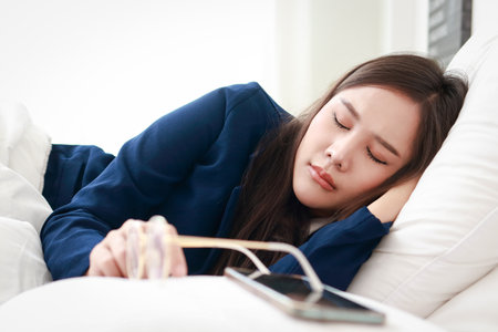 Asian women working hard Wearing a blue suit, sleeping on the bed with a smartphone in front of him. Business concept, Entrepreneurの写真素材