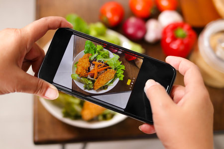 A man uses a black smartphone to take a picture of the food placed on the table. Food concept.