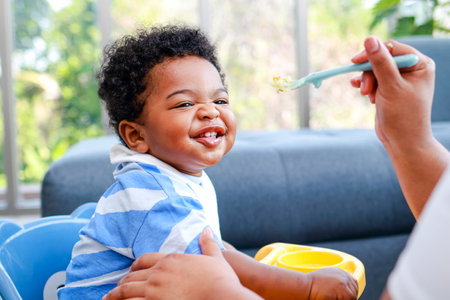 Happy smiling boy with mom while eating in the living room at home. Preschool child development, food menu for 1 year oldsの写真素材