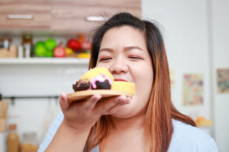 Asian fat woman eating delicious chocolate dessert in hand. Healthy eating concept. Weight loss. Happy woman likes to eat.の写真素材