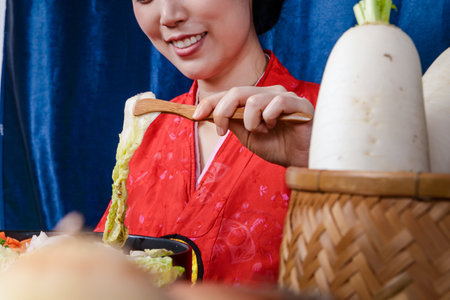 A beautiful Korean woman wearing a beautiful hanbok is making kimchi. Concept of Korean national costume. Fermented foodの写真素材