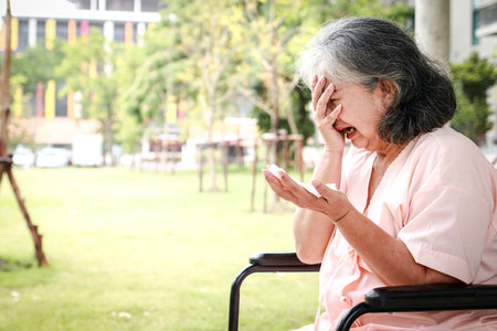 An elderly Asian female patient sits in a wheelchair in a hospital, she regrets her illness. Elderly disease concept, health insurance. copy spaceの写真素材