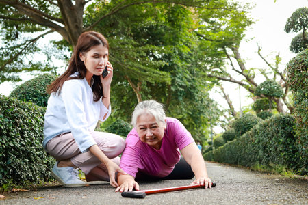Asian woman helping an elderly person lying on the road Call for an emergency ambulance. Health concept, insuranceの写真素材
