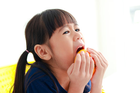 An Asian little girl is eating a very sour orange. food nutrition concept for kidsの写真素材