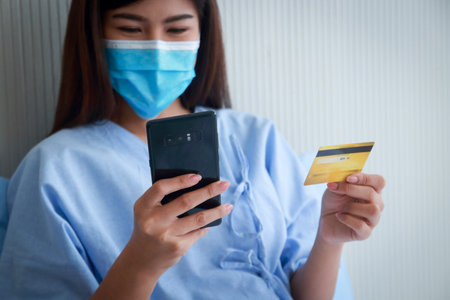 Asian female patient holding smartphone and credit card to pay medical bills. Finance concept, health insurance.の写真素材