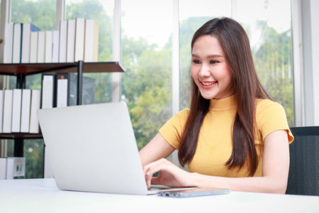 Beautiful smiling Asian female worker sitting in the office using a laptop computer to work. business people conceptの写真素材