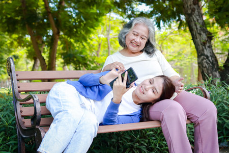 An elderly mother and her daughter relax on a bench in the park. They smile happily. Family concept. health care, life insuranceの写真素材