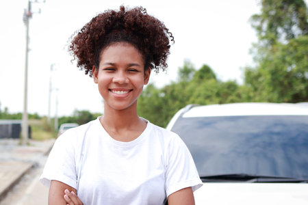 Portrait of a beautiful smiling African American woman standing in front of a car with arms crossed. Transportation concept. car insuranceの写真素材