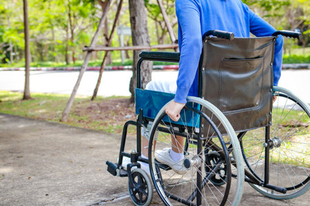 woman sitting in a wheelchair Use your own hand to spin the wheel and enjoy the park in the morning. urban lifestyleの写真素材