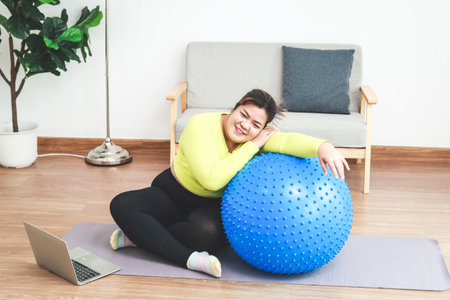 Asian fat woman exercising at home, she sits on a yoga mat and leans on a yoga ball. Health care, weight loss. sports conceptの写真素材