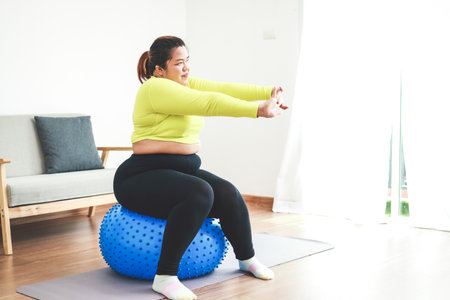 Asian woman exercising at home She sits on a yoga ball doing stretching poses. Sports concept, healthy lifestyle.の写真素材