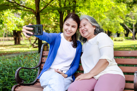 Asian family concept. Caring for the elderly to be happy. An elderly mother and her daughter take pictures playing in an outdoor park. They smile happily.の写真素材