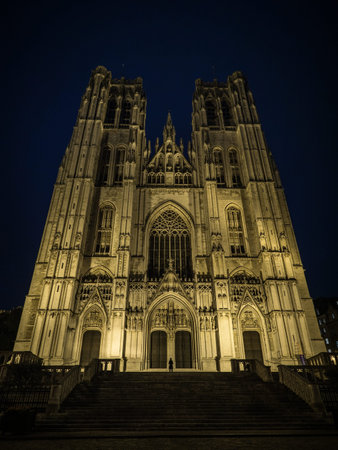 Person infront of illuminated facade of gothic catholic church cathedral of St Michael and St Gudula in Brussels Belgiumの写真素材