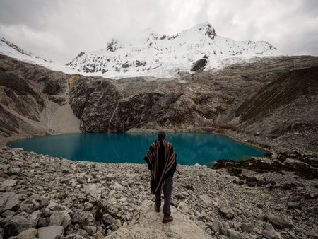 Hiker in traditional indigenous poncho cape at andean mountain lake Laguna 69 Cordillera Blanca...