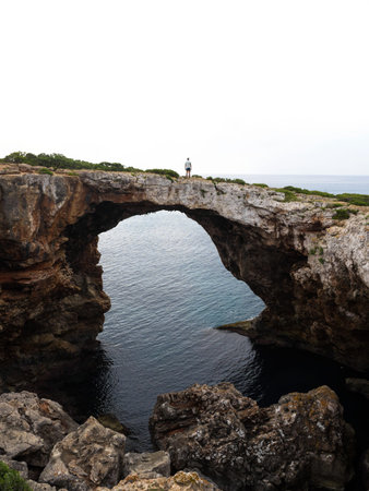 Male person tourist hiker man on natural arch rock bridge at Cala Varques Calo Blanc Mallorca Mediterranean sea Spainの写真素材