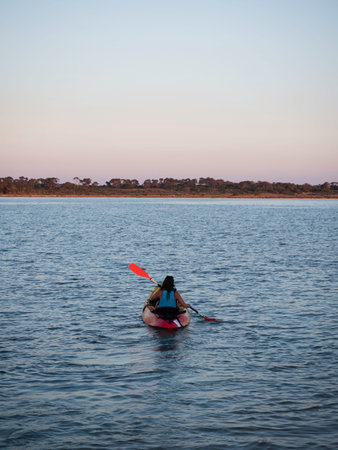 Young female person woman girl in red yellow kayak paddling into sunset clear blue ocean water Mallorca Spainの写真素材
