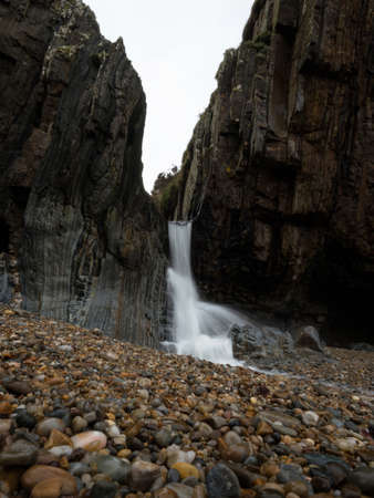 Waterfall long exposure at Playa del Silencio Gavieiro beach ocean sea coast shore cliffs in...