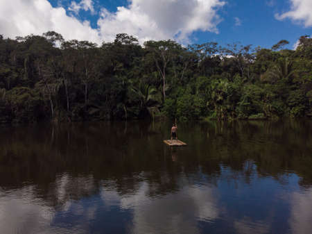 Young man standing on wooden raft float on tropical exotic Amazon rainforest jungle water lake river near Sauce lagoon Tarapoto Peru South Americaの写真素材