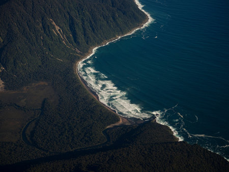 Airplane window panorama view of the untouched wilderness of Southland, majestic Southern Alps foothill mountain meeting rough pacific ocean shore coastline South Island New Zealandの写真素材
