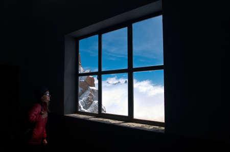 Woman in the dark staring at a blue sky through a windowの写真素材