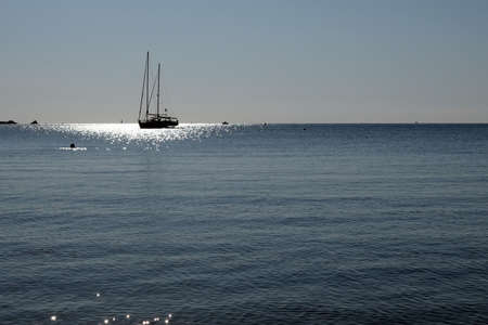 Sailboat at anchor in France in a summer during a hot and sunny day, calm sea, blue sky and sun reflexesの写真素材