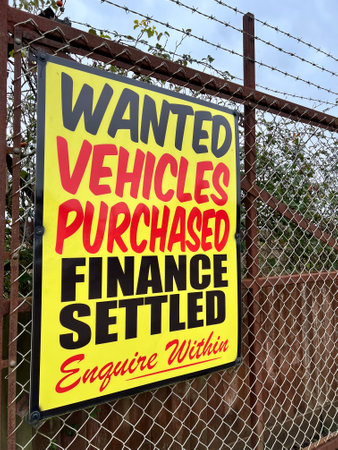 Signage reading âWanted, Vehicles Purchased, Finance Settled, Enquire Withinâ mounted on the rusted metal fencing of a used car garage forecourt.の写真素材