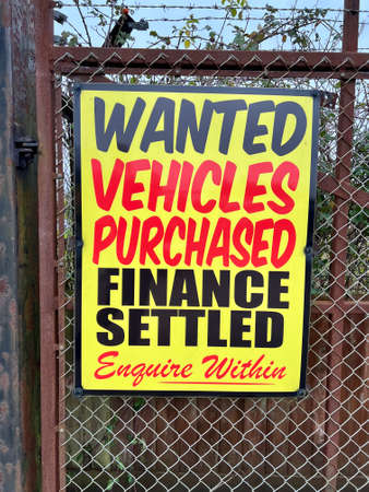 Signage reading âWanted, Vehicles Purchased, Finance Settled, Enquire Withinâ mounted on the rusted metal fencing of a used car garage forecourt.の写真素材