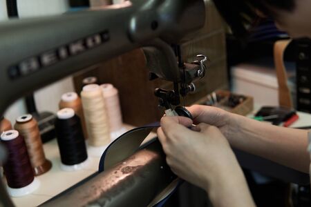 the hand of a woman sewing leather with a sewing machine