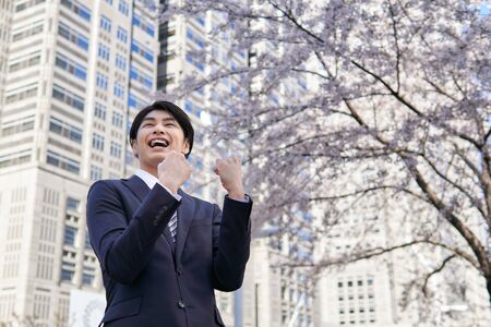 Japanese male businessman posing in a guts ye in the background of cherry blossoms in the office districtの写真素材