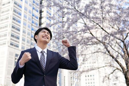 Japanese male businessman posing in a guts ye in the background of cherry blossoms in the office districtの写真素材