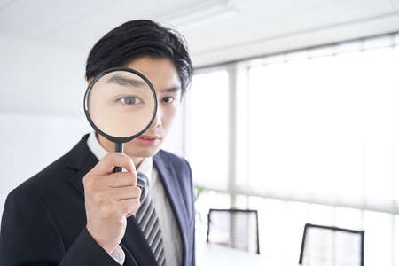 Japanese male businessman looking into a magnifying glass in a conference roomの写真素材